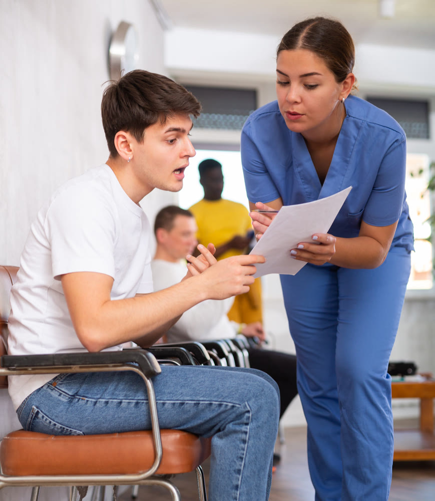 Dissatisfied surprised young man discussing documents with a doctor in the lobby of medical clinic