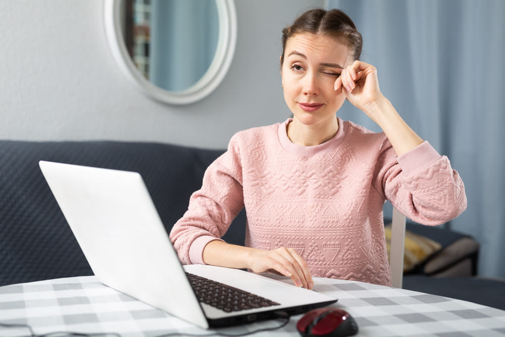 Young woman rubbing her eyes, using laptop in home office