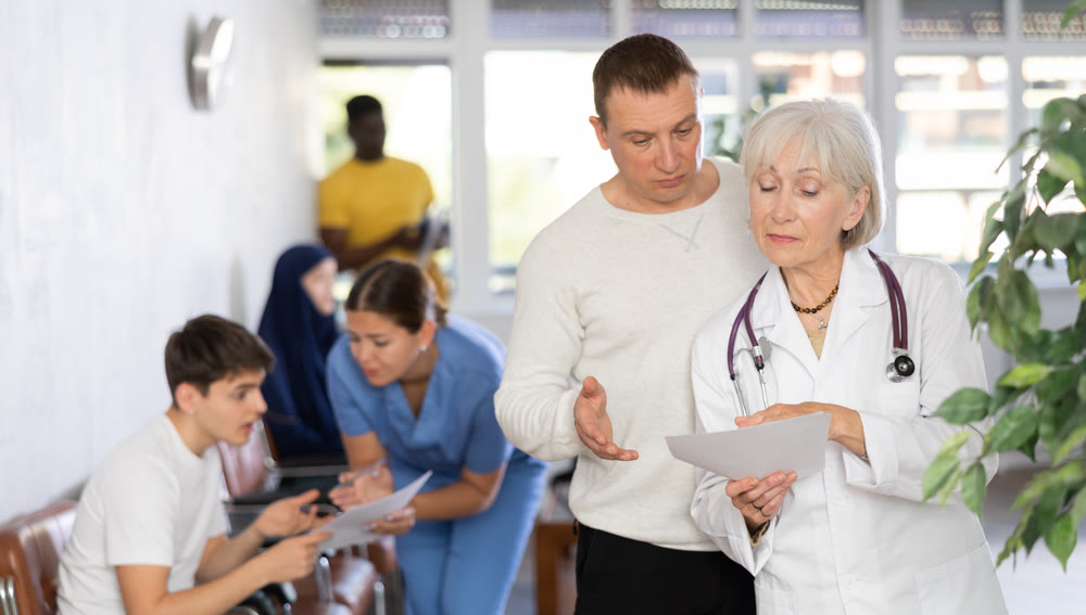 Elderly female doctor asking man to fill out paperwork in clinic