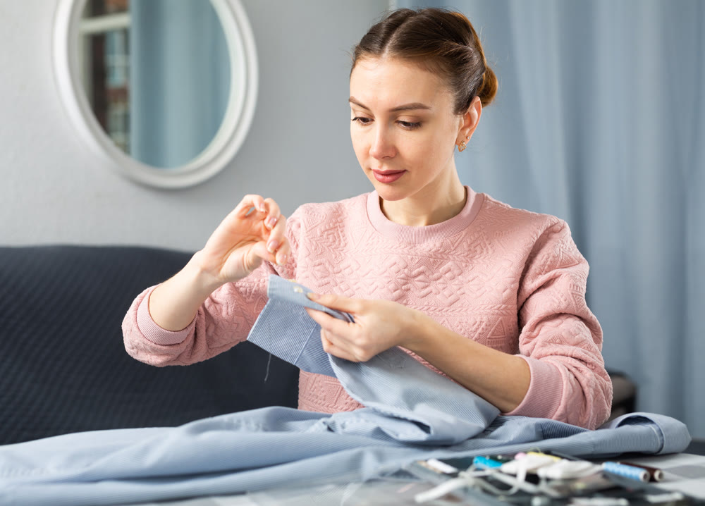 Young woman sewing on button at home