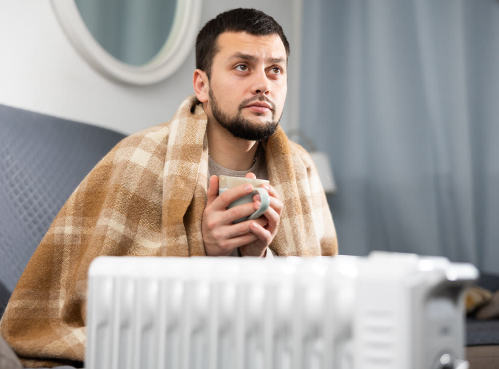 Adult man with cup near heater in home closeup