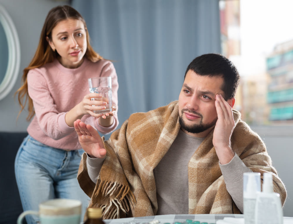 Young man with headache refusing help from caring wife