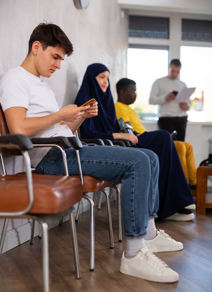 Guy teenager waiting in line at reception with phone in his hand