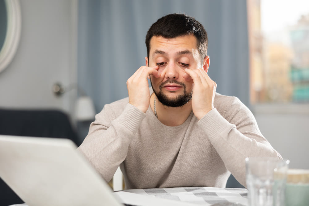 Young man rubbing tired eyes while working on computer at home