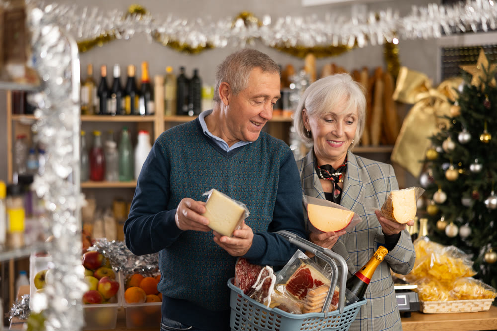 Elderly couple with a basket of groceries buys tasty cheese in grocery store