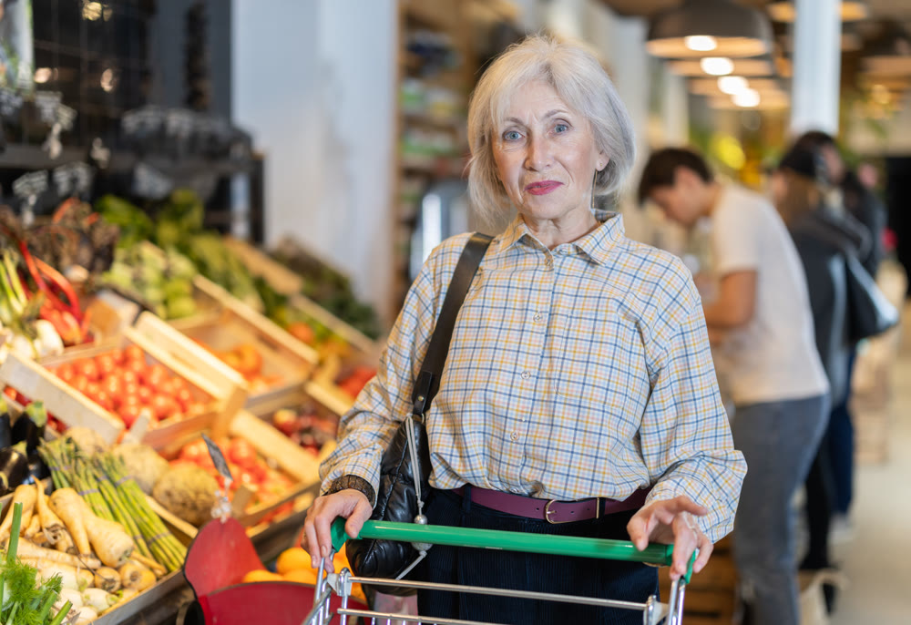Elderly woman with shopping cart chooses groceries