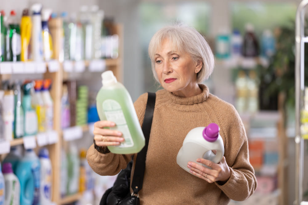 Mature positive woman consumer with household chemical products for washing indoors