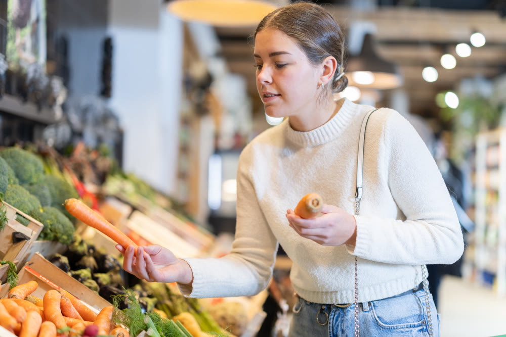 Young woman choosing carrots in grocery supermarket