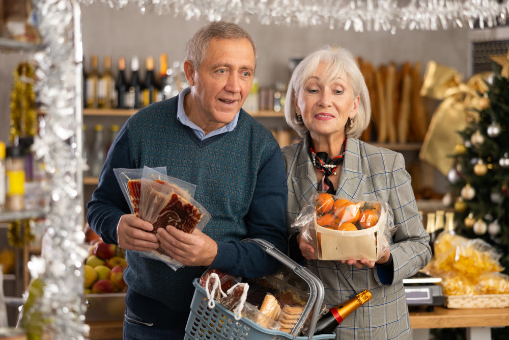 Elderly married couple prepares to celebrate Christmas - husband and wife choose dried jamon and tangerines together at supermarket