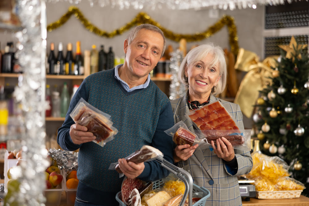 Mature couple with a basket of groceries buys dried sausage and ham in supermarket