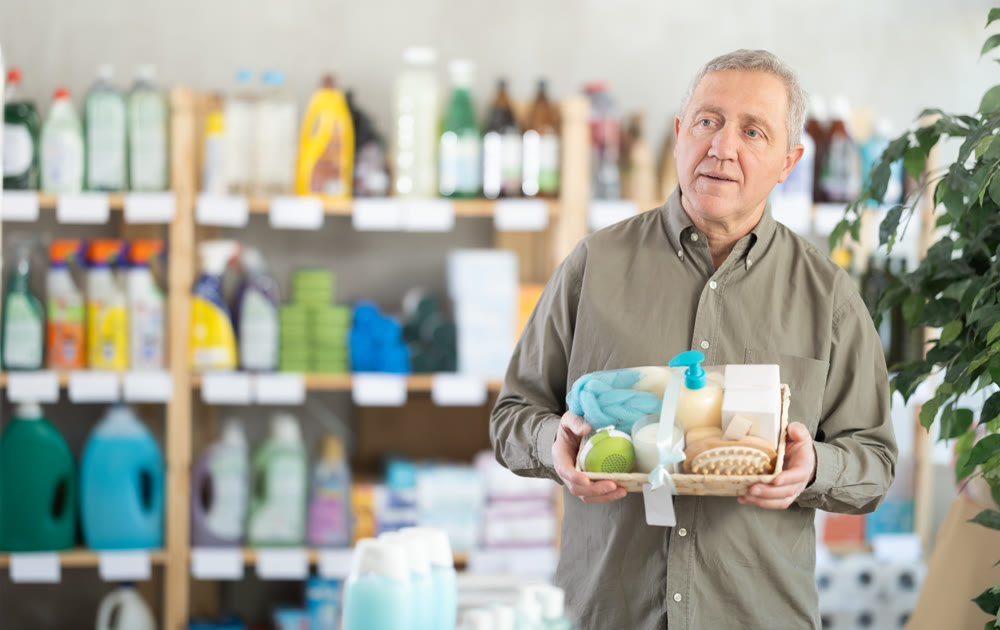 Senior man studies label and choose shower cosmetic present, packaged in basket.