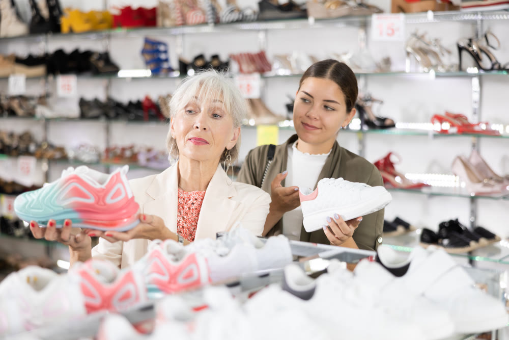 Elderly woman and young woman choosing sneakers in shoe store