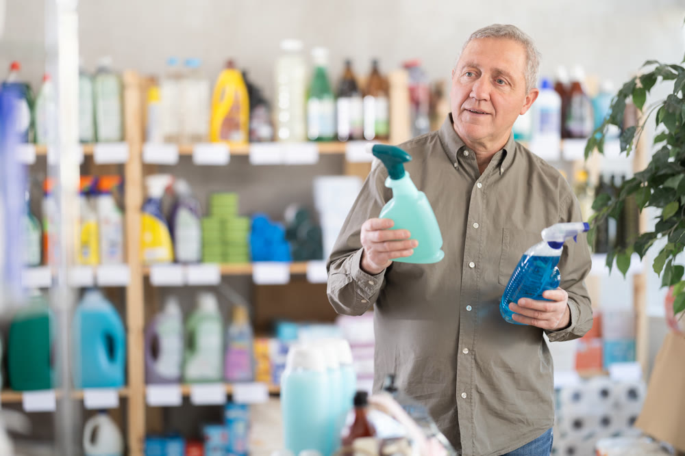 Elderly man choosing cleaning spray in supermarket