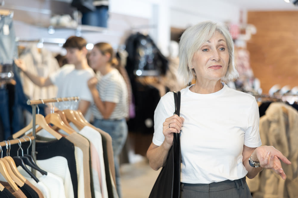 Old woman watching excitedly large stock of clothes in clothing store