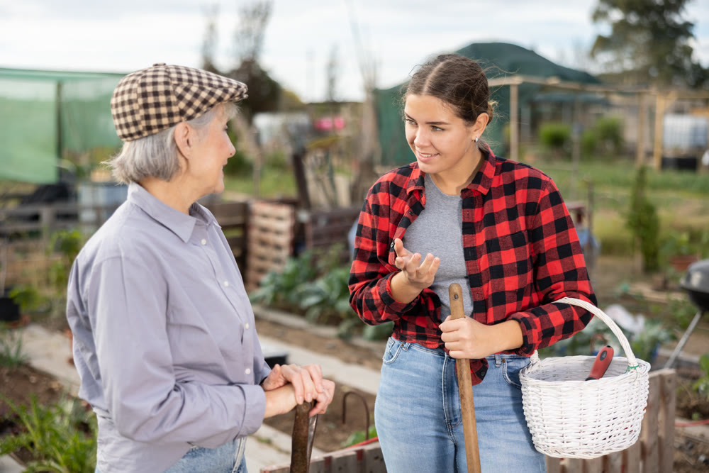 Two female gardeners talking near wooden fence in garden