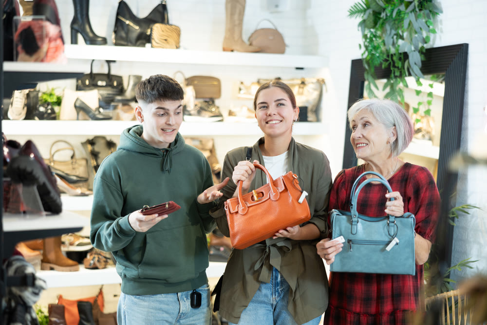 Mature woman sales consultant helps couple customers decide on choice of model handbag