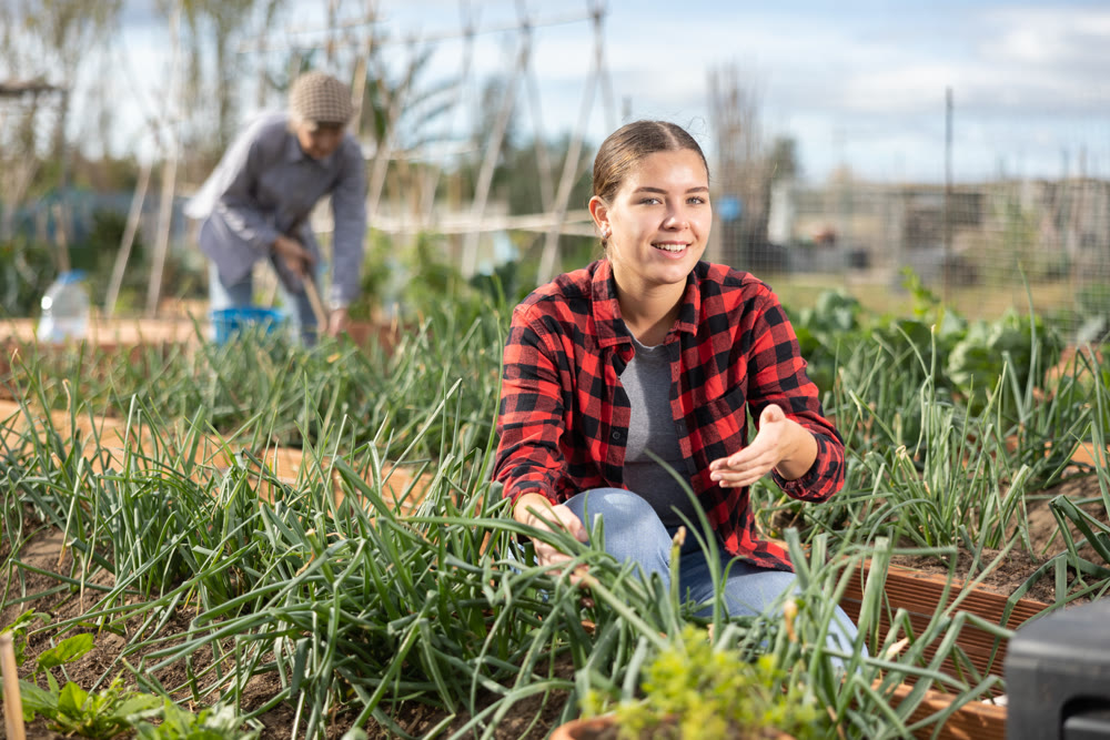 Smiling young woman caring for green onion sprouts in garden during daytime in March