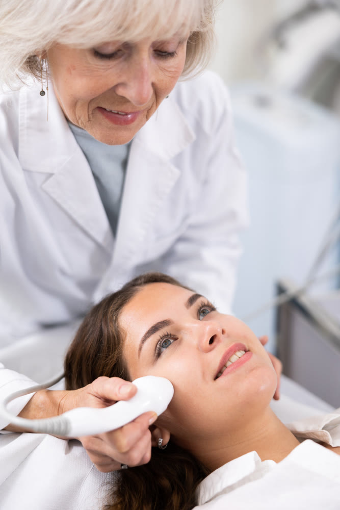 Young woman having face laser therapy procedure by specialist