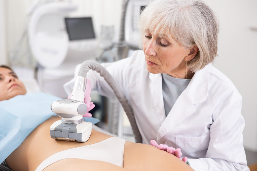 Young woman getting ultrasound cavitation body contouring treatment, anti-cellulite therapy, vacuum massage from old female cosmetologist. Hardware cosmetology for body sculpting