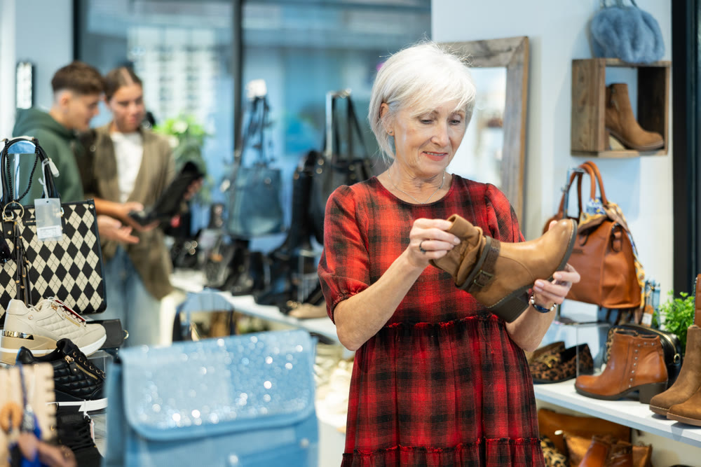 Elderly woman buyer looks at footwear from new collection and picks up new pair of boots for winter.