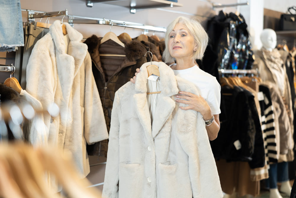 Old woman choosing white fur coat in clothing shop