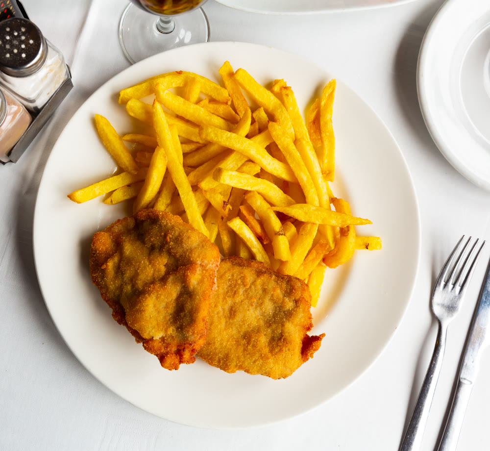 Appetizing breaded pork steak baked in oven with golden french fries