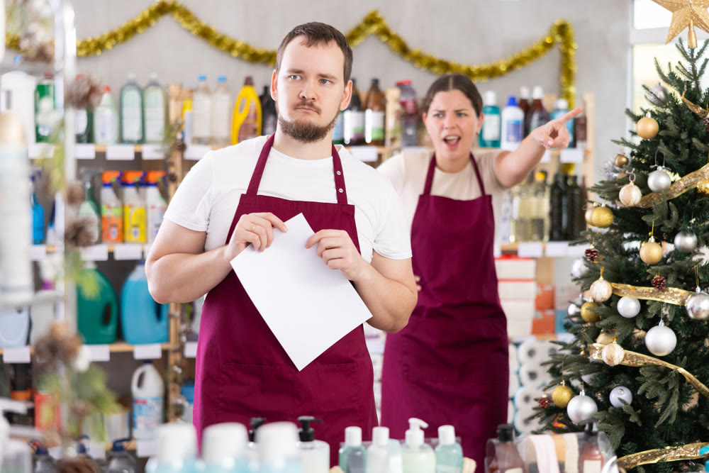 Angry saleswoman scolding at male assistant in hardware store decorated for New Year celebration