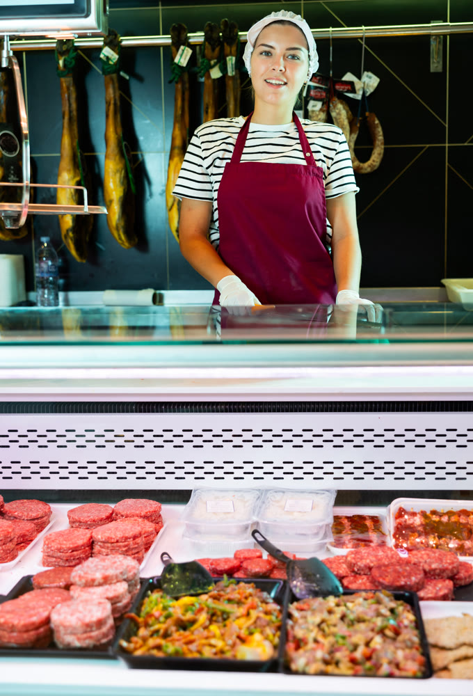 Smiling female butcher holding meat cutlets in meat section of grocery