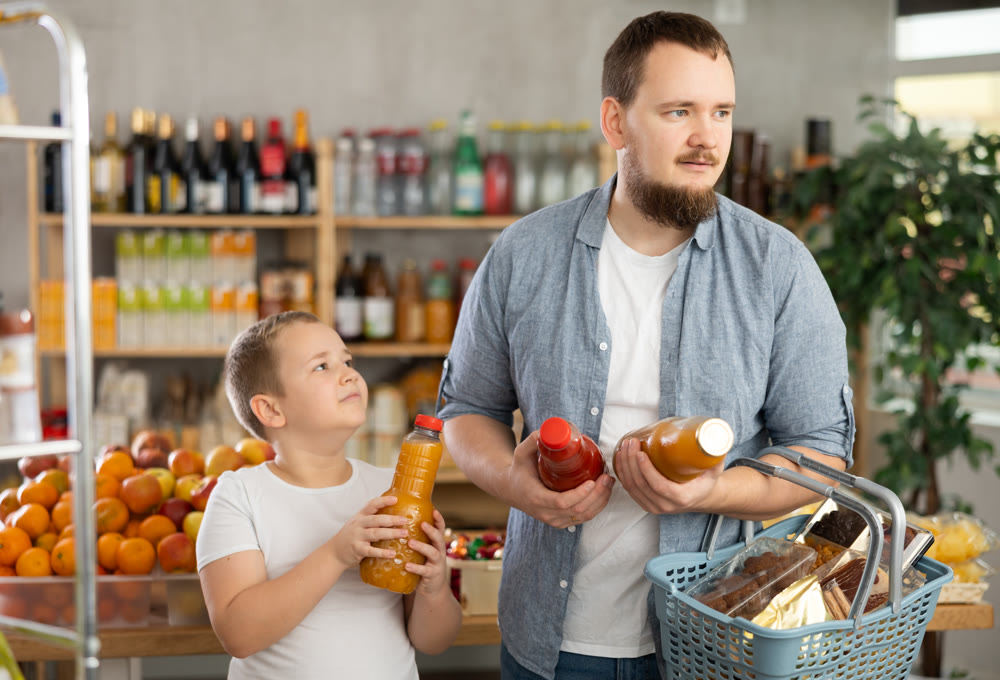 Man with son hold packages plastic bottle and choose consider fruit juice in store