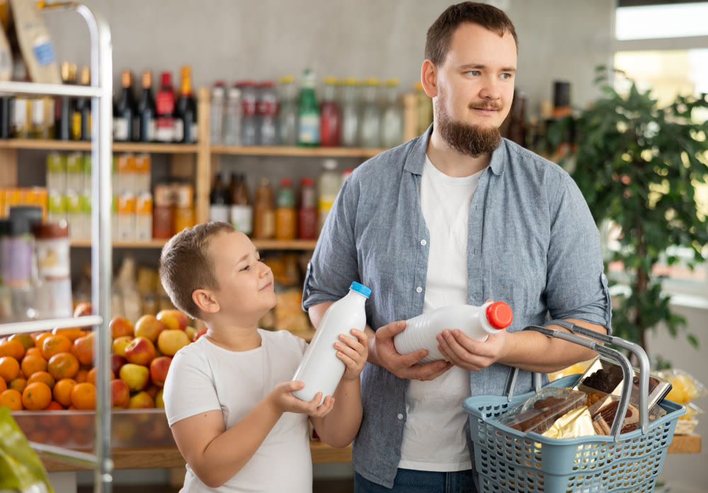 Young man with tween son choosing organic bottled milk in store