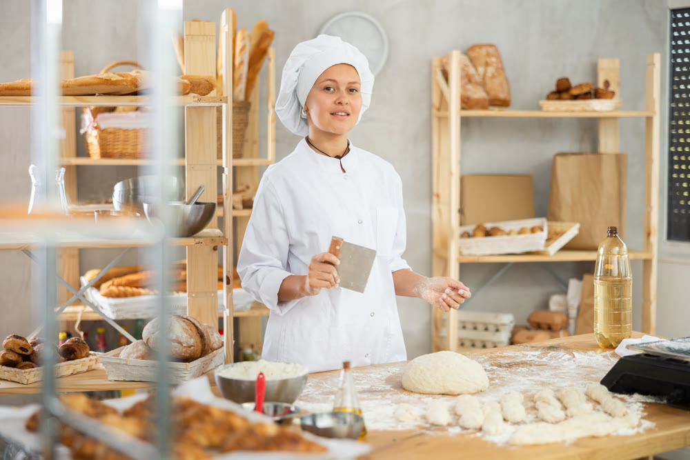 Female baker in uniform cutting raw dough with knife to make croissants or buns