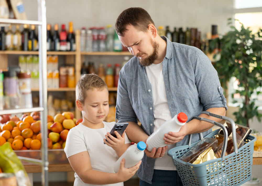 European man with son customer at shop scans QR code on milk bottle using phone camera