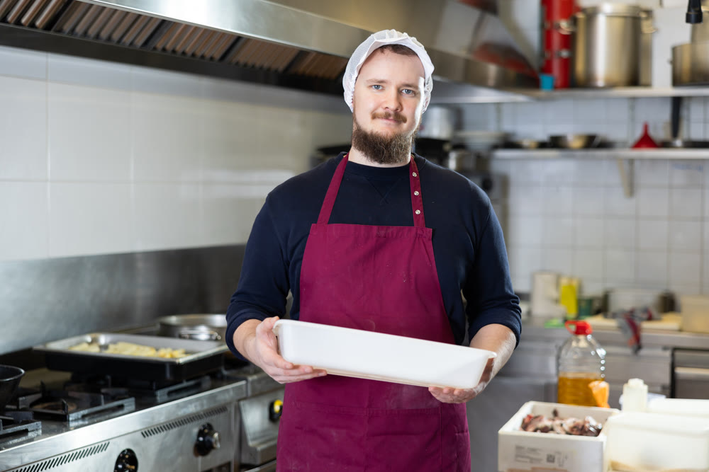 Male cook prepares chicken legs - cuts them with knife before cooking