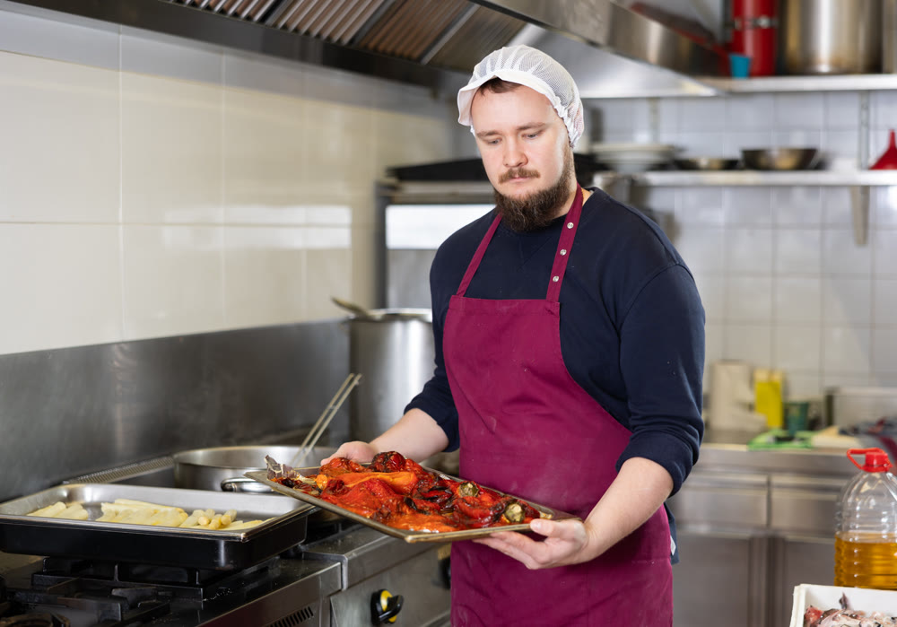 Bearded chef preparing vegetable dishes for sale in deli section of store