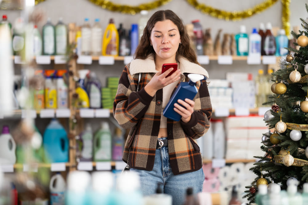 Young girl scanning QR-code on cleaning spray in store during Christmas