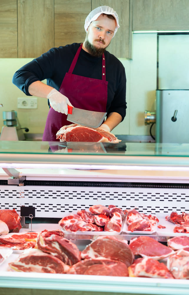 Butcher cuts piece of raw meat for sale in the meat department of supermarket