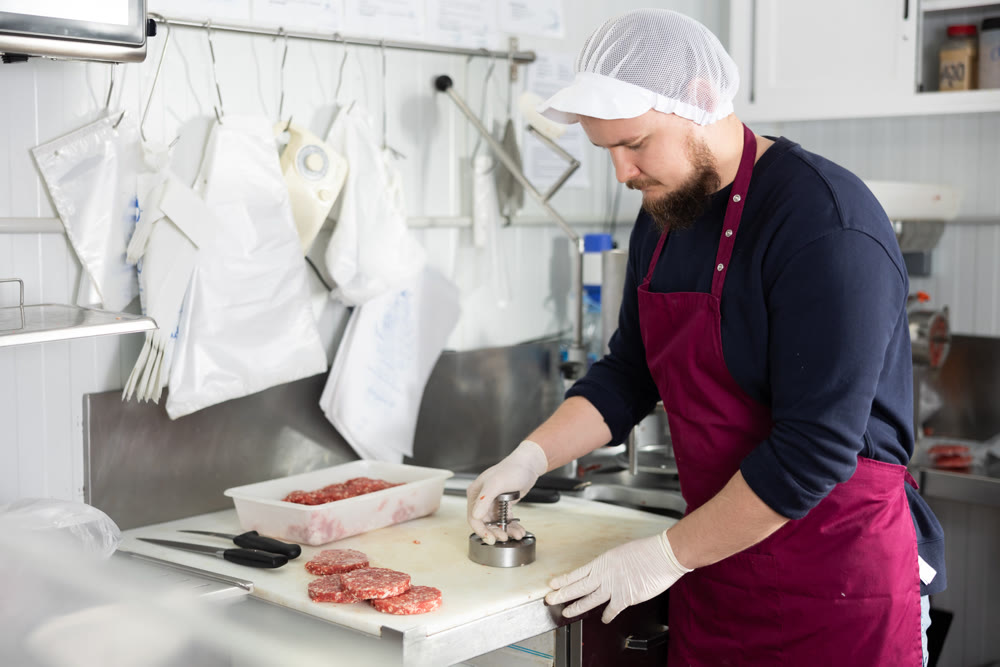 Bearded butcher shaping ground veal burger patties for sale in shop