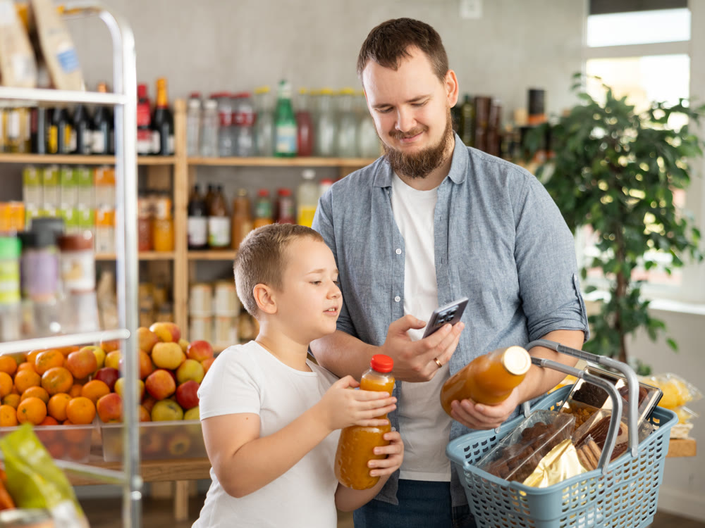 Boy with father scanning barcodes on bottles with juices with phone in supermarket