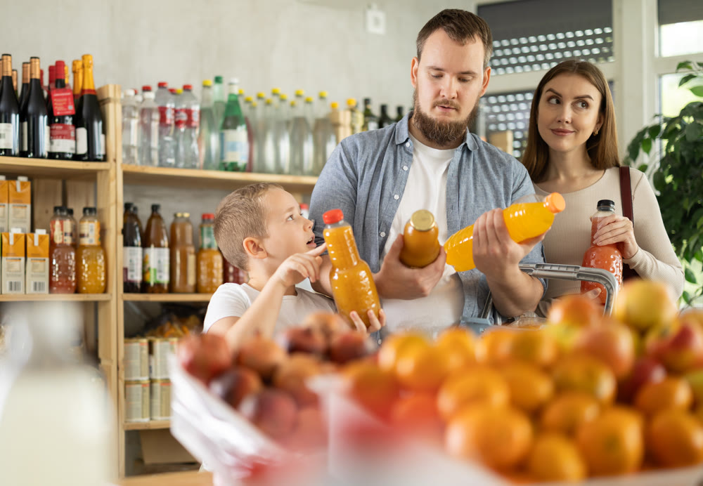 Young family with little son choosing natural juice in supermarket