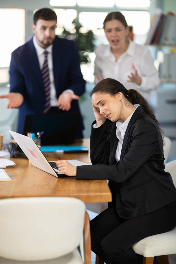 Group of people scolding sad colleague sitting at laptop in office