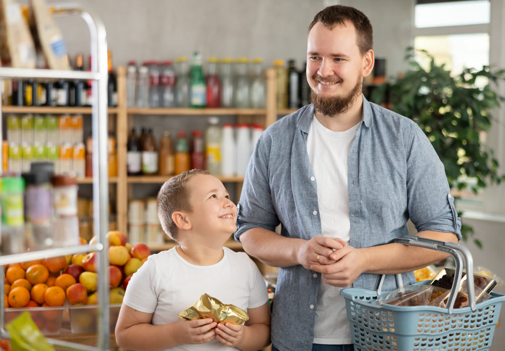 Young dad and tween son choosing food together in supermarket