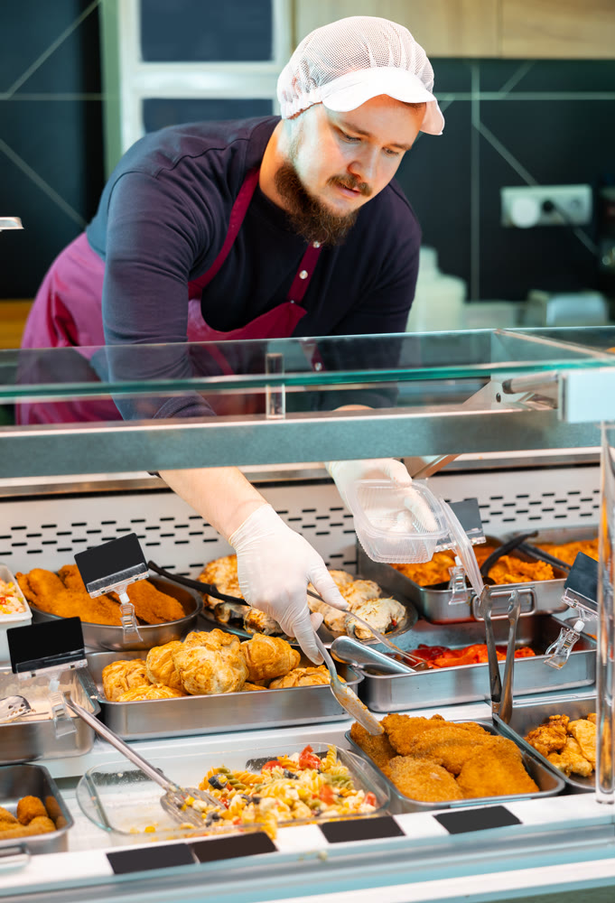 Salesman serving ready-to-eat dishes from deli counter in supermarket