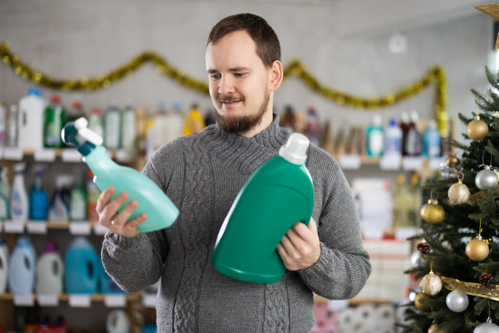 Bearded man customer buying spray and detergent in store decorated for New Year holiday