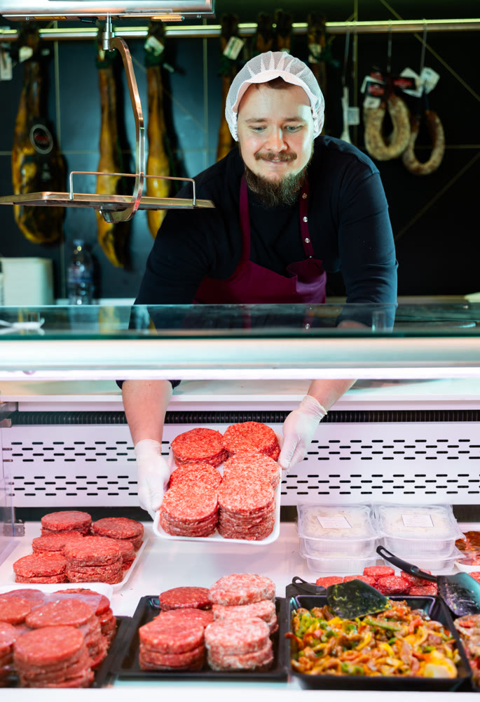 Man butcher holding meat cutlets in meat section of supermarket