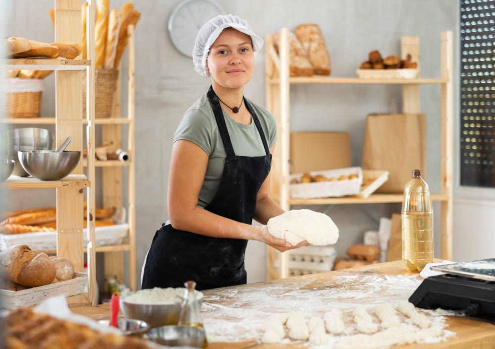 Working in bakery - girl kneads raw dough to make baguettes or croissants