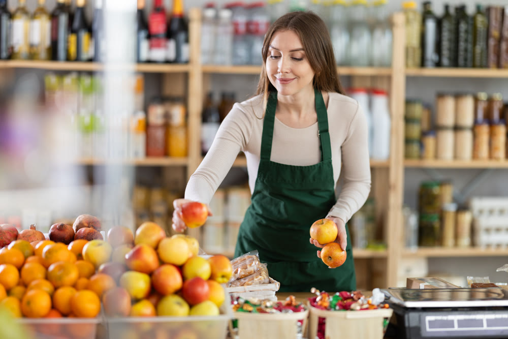 Young saleswoman putting apples on display in grocery