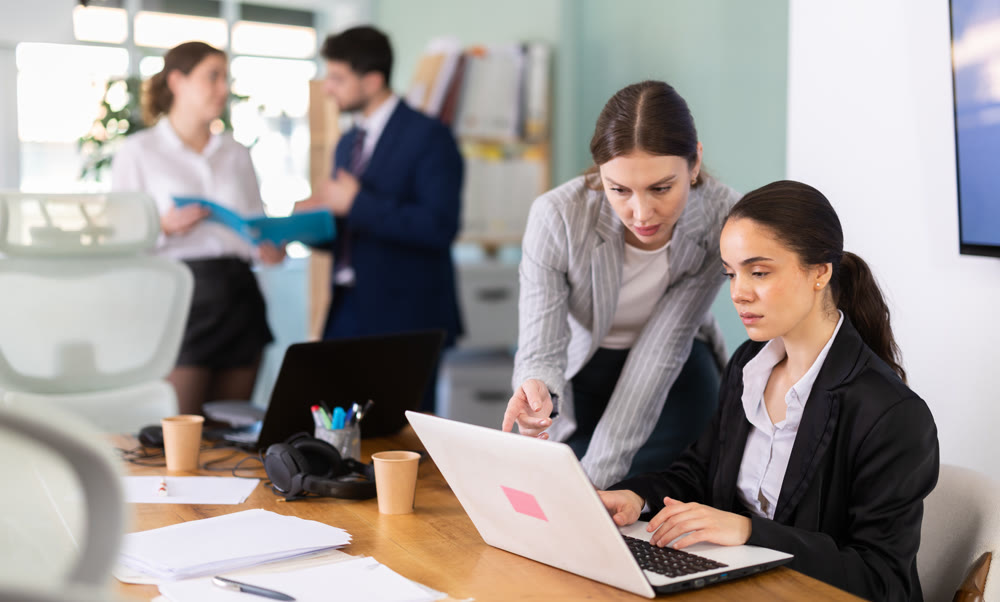 Young woman helping female colleague work on laptop