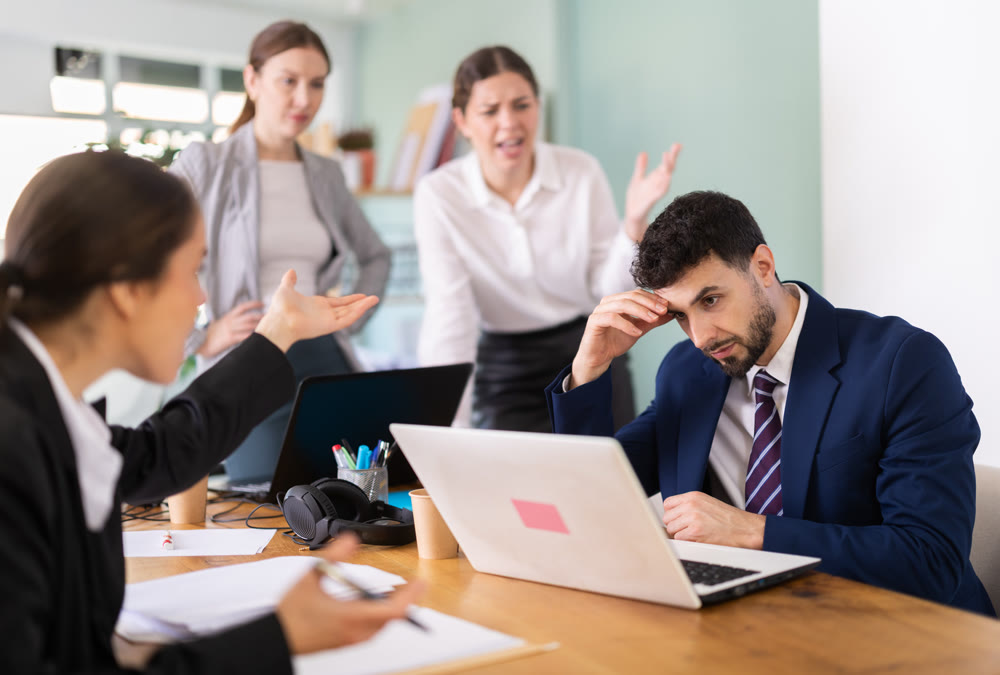 Group of colleagues scolding sad man in office