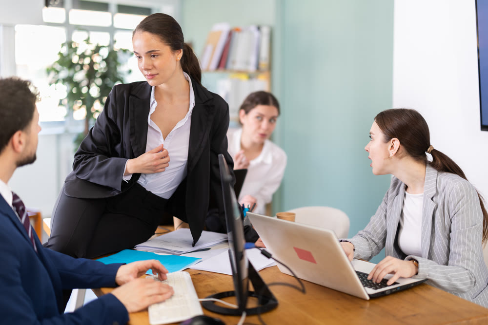 Young woman flirting with male colleague while sitting on office desk
