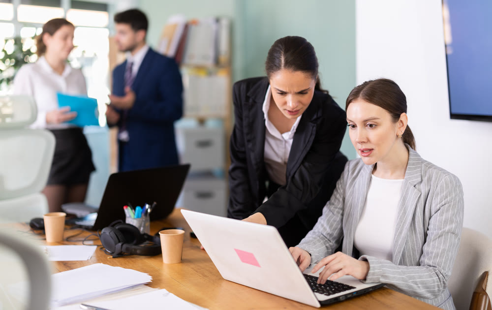 Young girl helping colleague with tasks on laptop